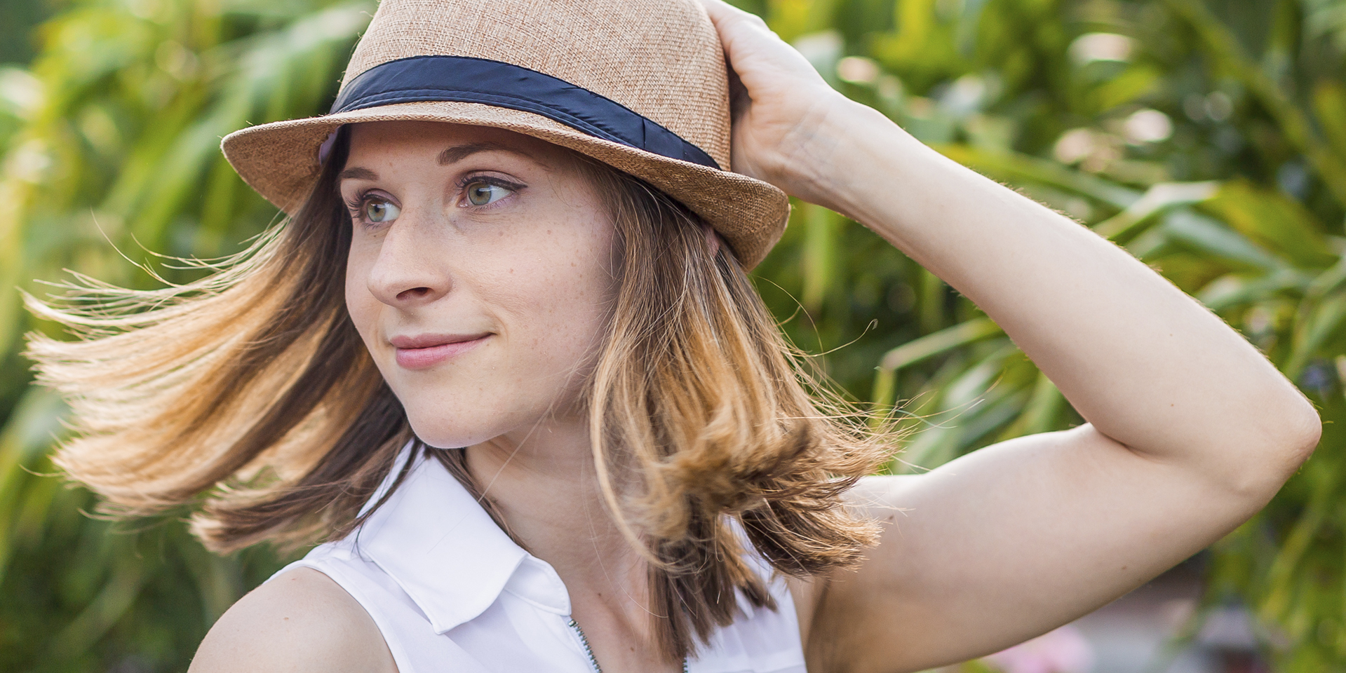 Close picture of Dr. Kara Larson smiling with a hand on the back of her head holding her hat with a green nature background. Book Dr. Kara Larson—leadership & mental wellness speaker—for transformative talks on productivity, burnout prevention, and peak performance